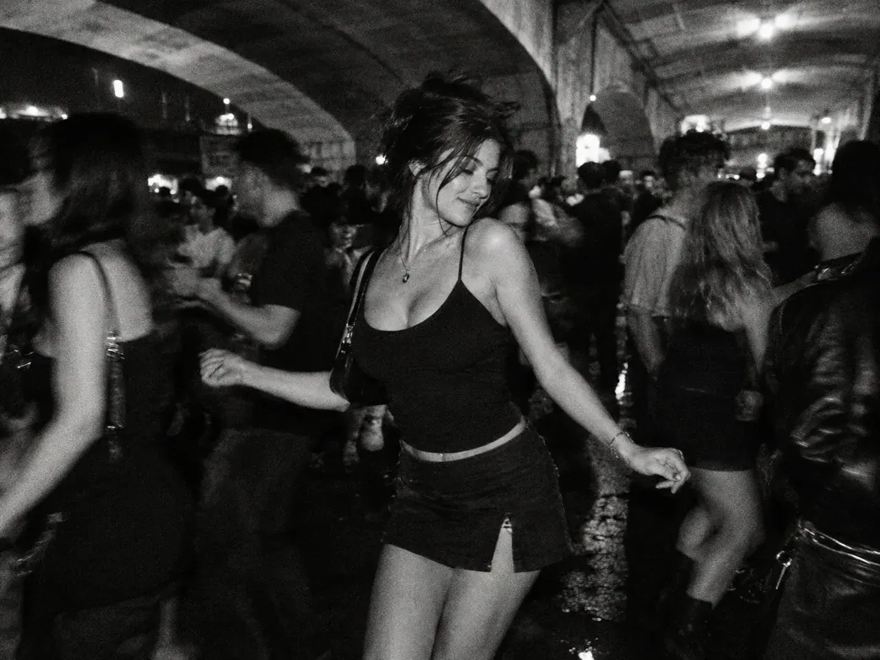 Grainy black-and-white film photograph of an adult dancing in a crowded night party