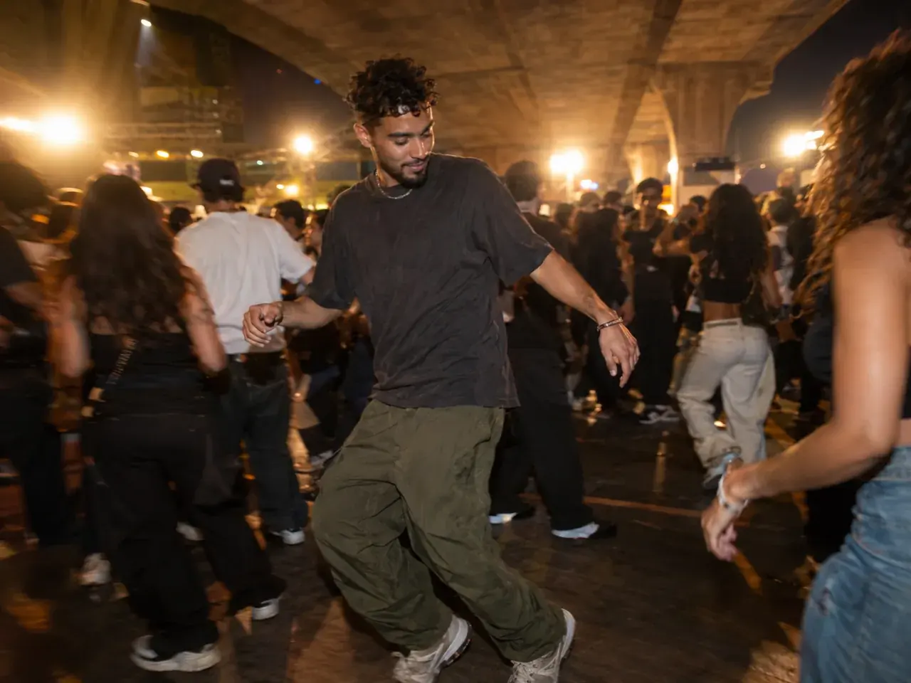 Adult in casual clothes dancing in a packed night street party under a concrete viaduct